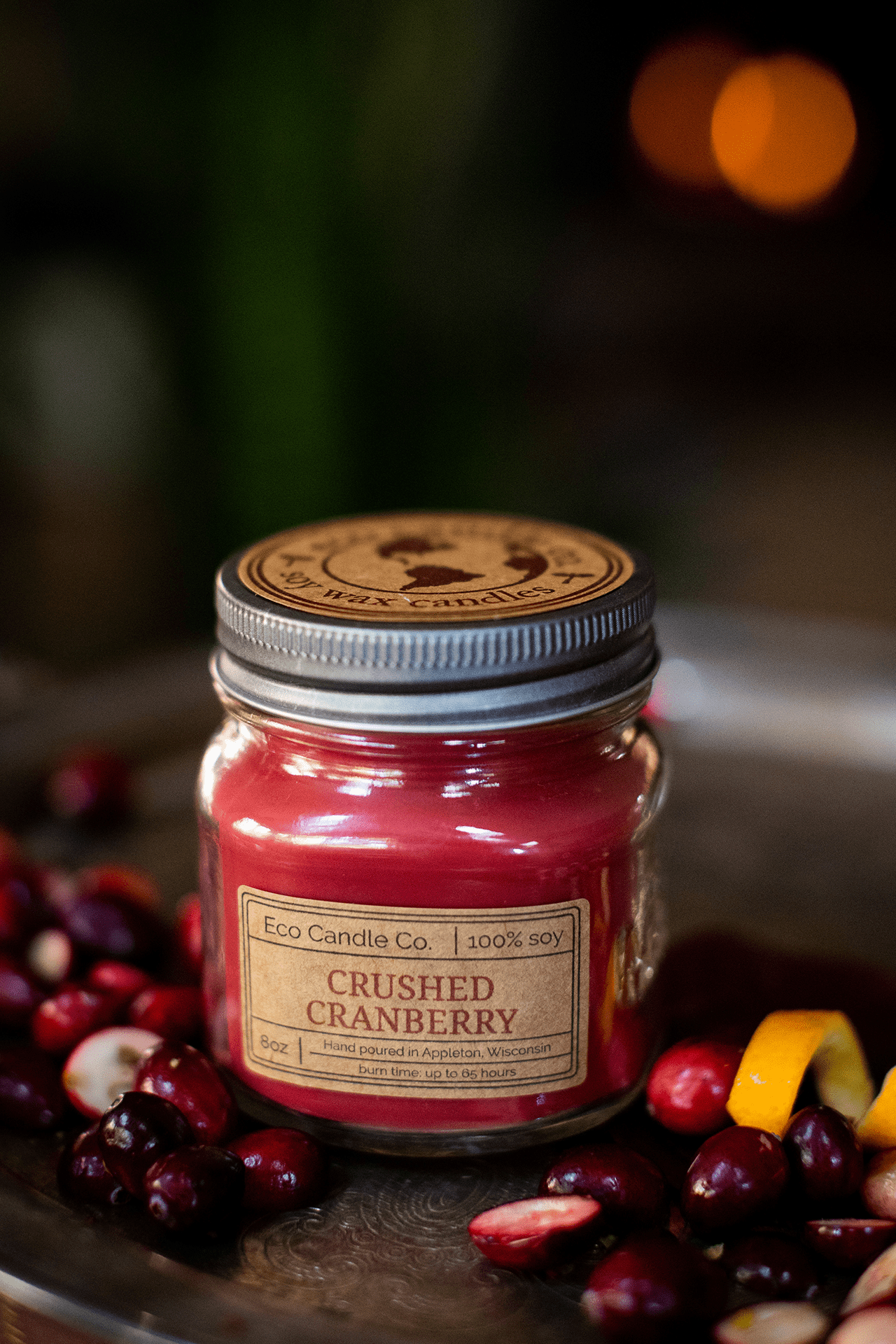 Crushed Cranberry Soy Candle by Eco Candle Company in a mason jar on a dark surface with cranberries and oranges.