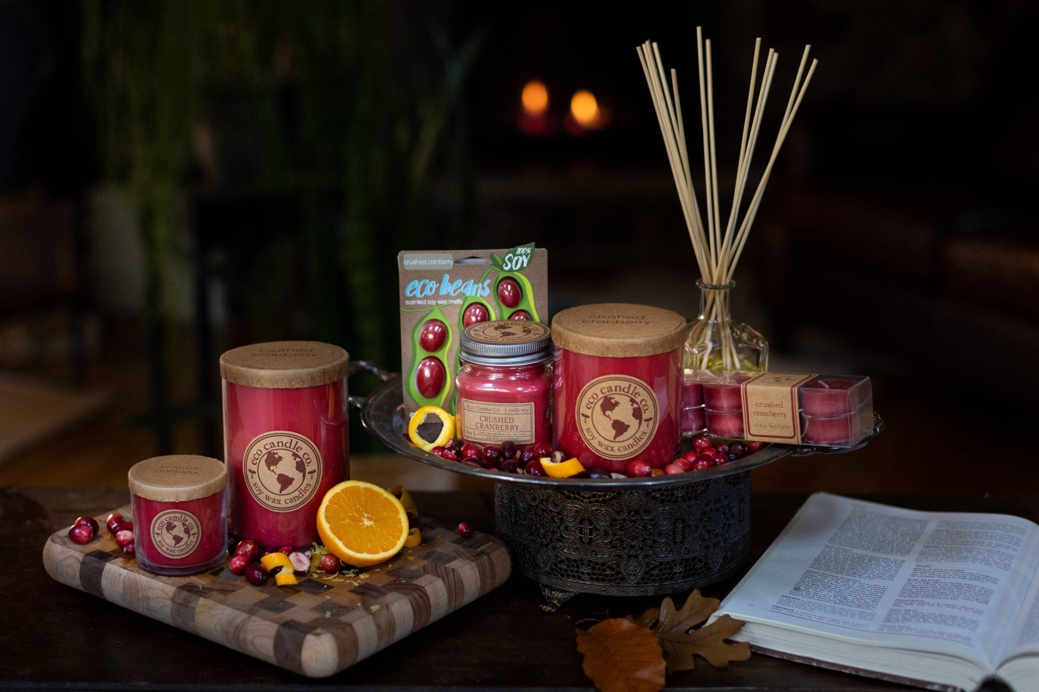 Assorted Crushed Cranberry Soy Candles and diffusers by Eco Candle Company on a dark surface with a warm glow.