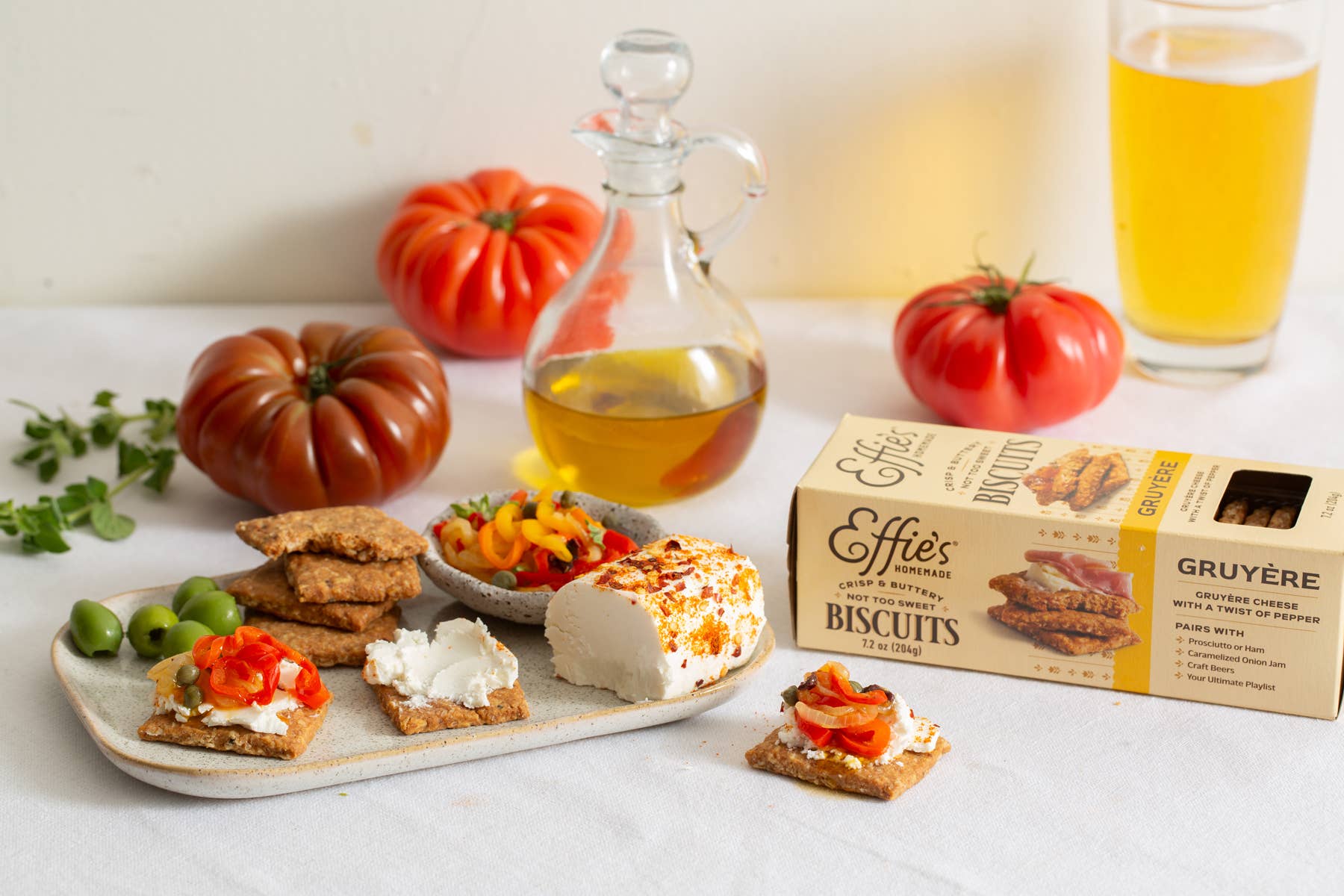 Platter of snacks with tomatoes, a bottle of oil, and a box of Effies Gruyère Biscuits on a table.