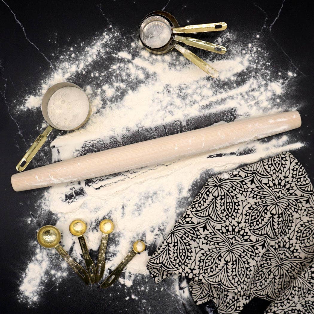 French Dowel Rolling Pin by J.K. Adams Company and measuring cups on a black surface with flour