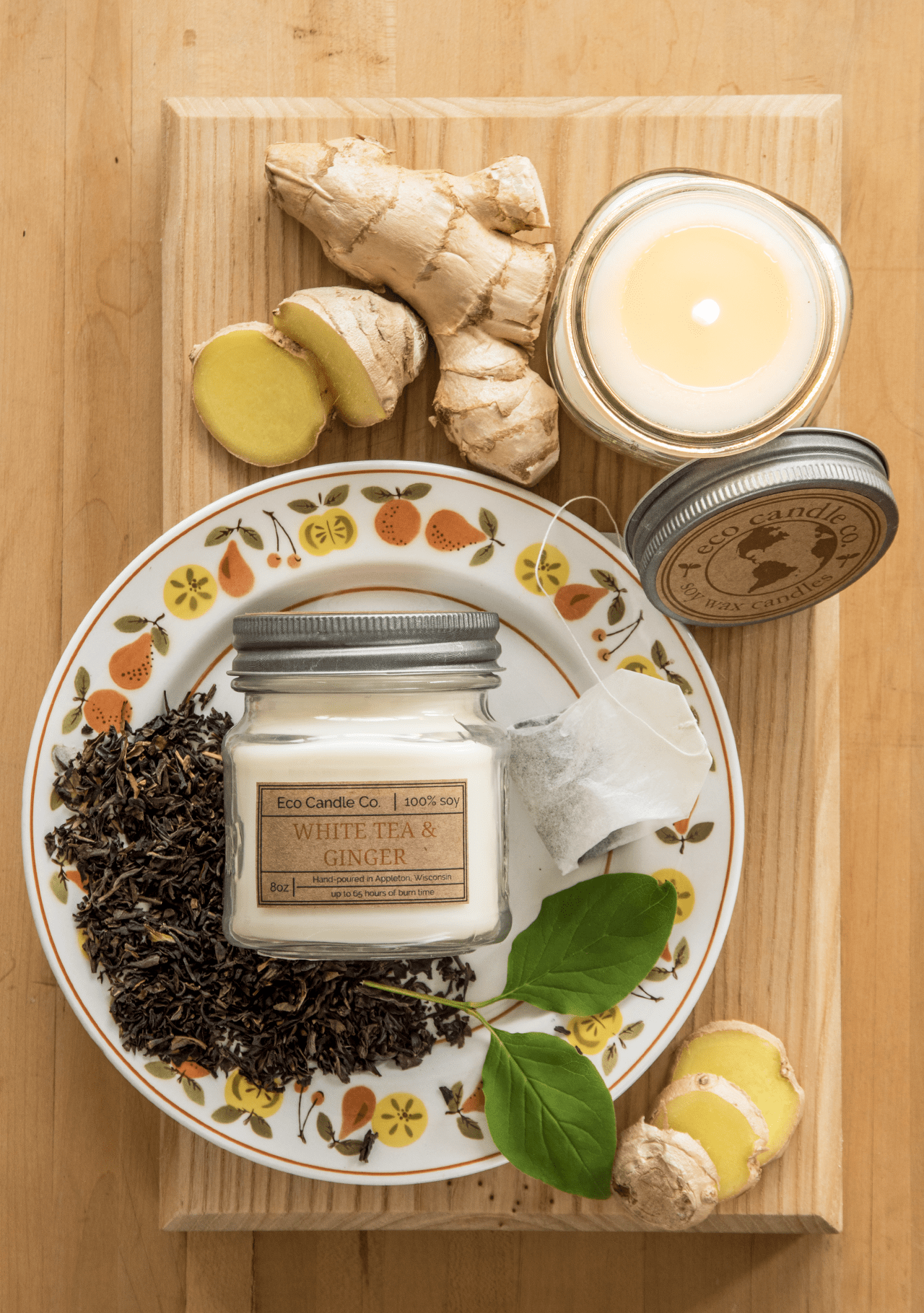 White Tea & Ginger Soy Candle by Eco Candle Co on a decorative plate with ginger and tea leaves on a wooden surface.