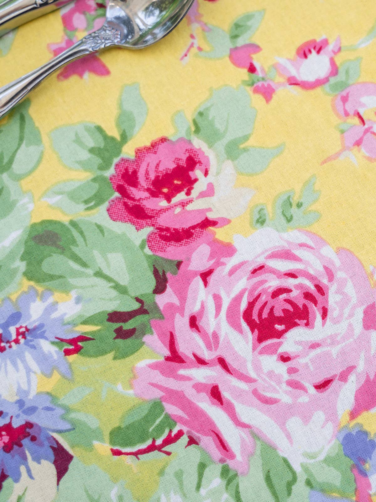 Close-up of the Yellow Cottage Rose tablecloth by April Cornell. The tablecloth features a yellow background with pink and periwinkle flowers.