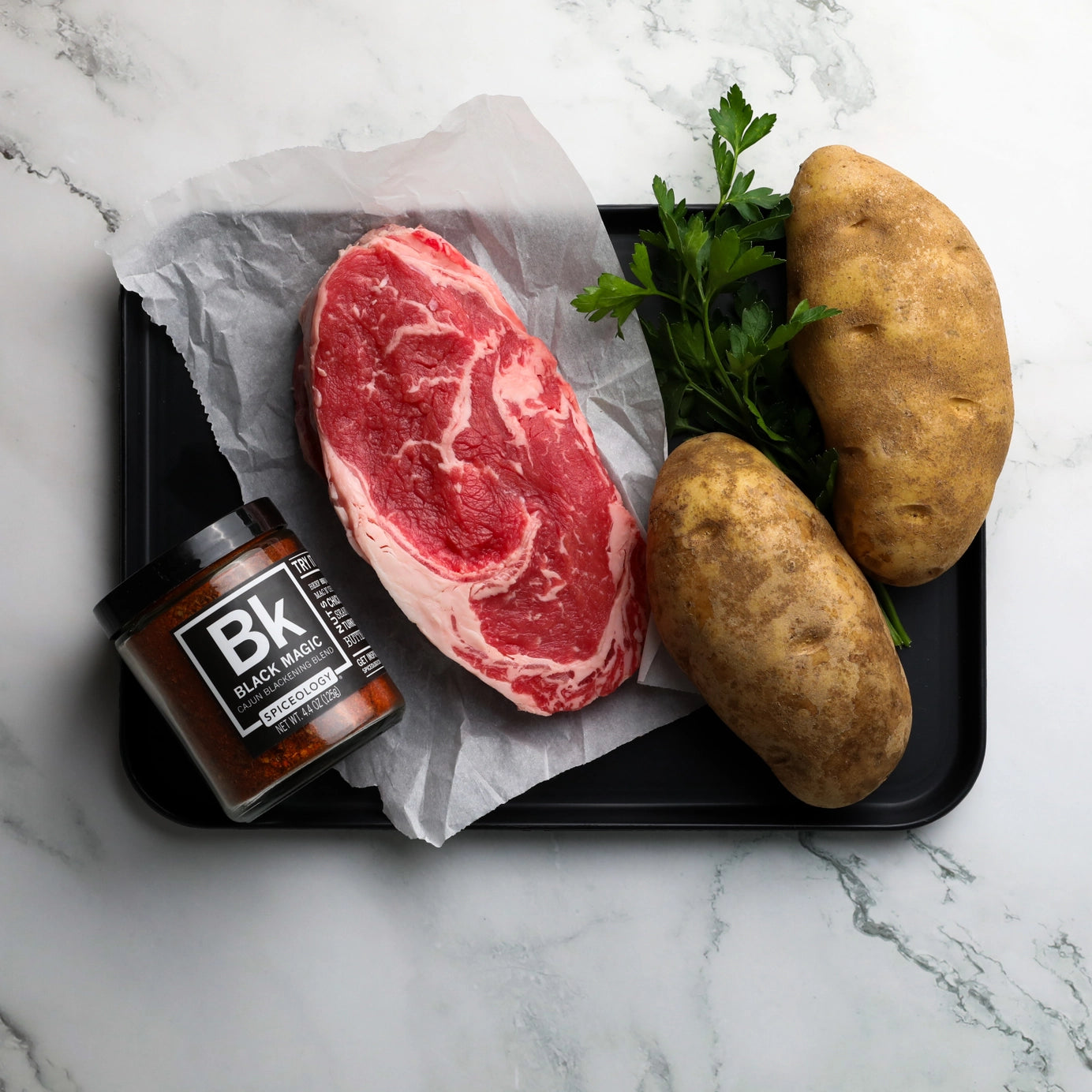 Steak and potatoes about to be seasoned with Black Magic Cajun Blackening Rub by Spiceology – a bold Cajun spice blend