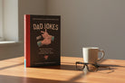 “The Essential Compendium of Dad Jokes” hardcover book displayed on wooden desk