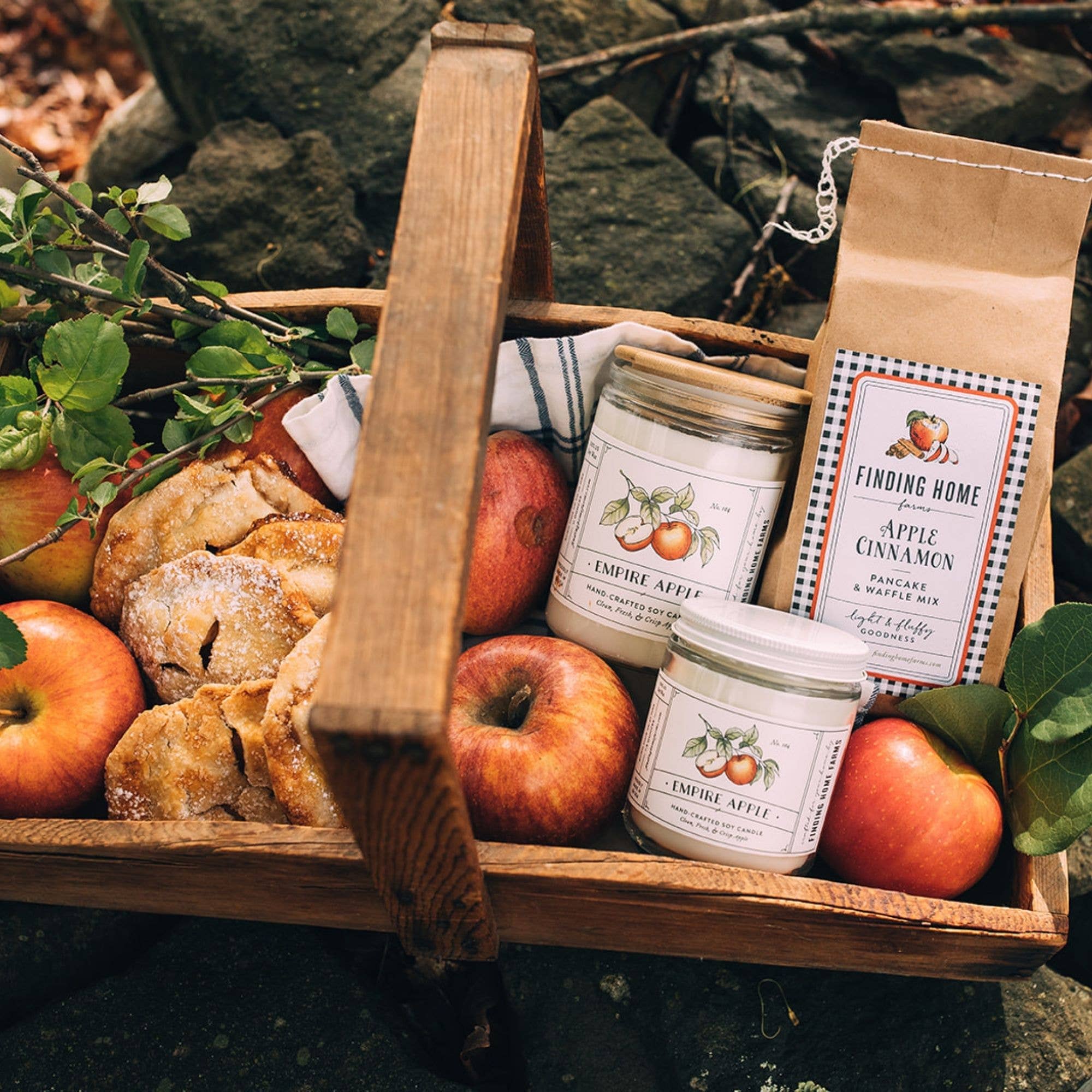 Wooden basket with apples, bread, Empire Apple Soy Candles, and Apple Cinnamon Pancake Mix from Finding Home Farms