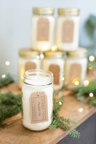 Fraser Fir Soy Candle by Eco Candle Company in glass jars on a wooden surface with greenery and lights in the background