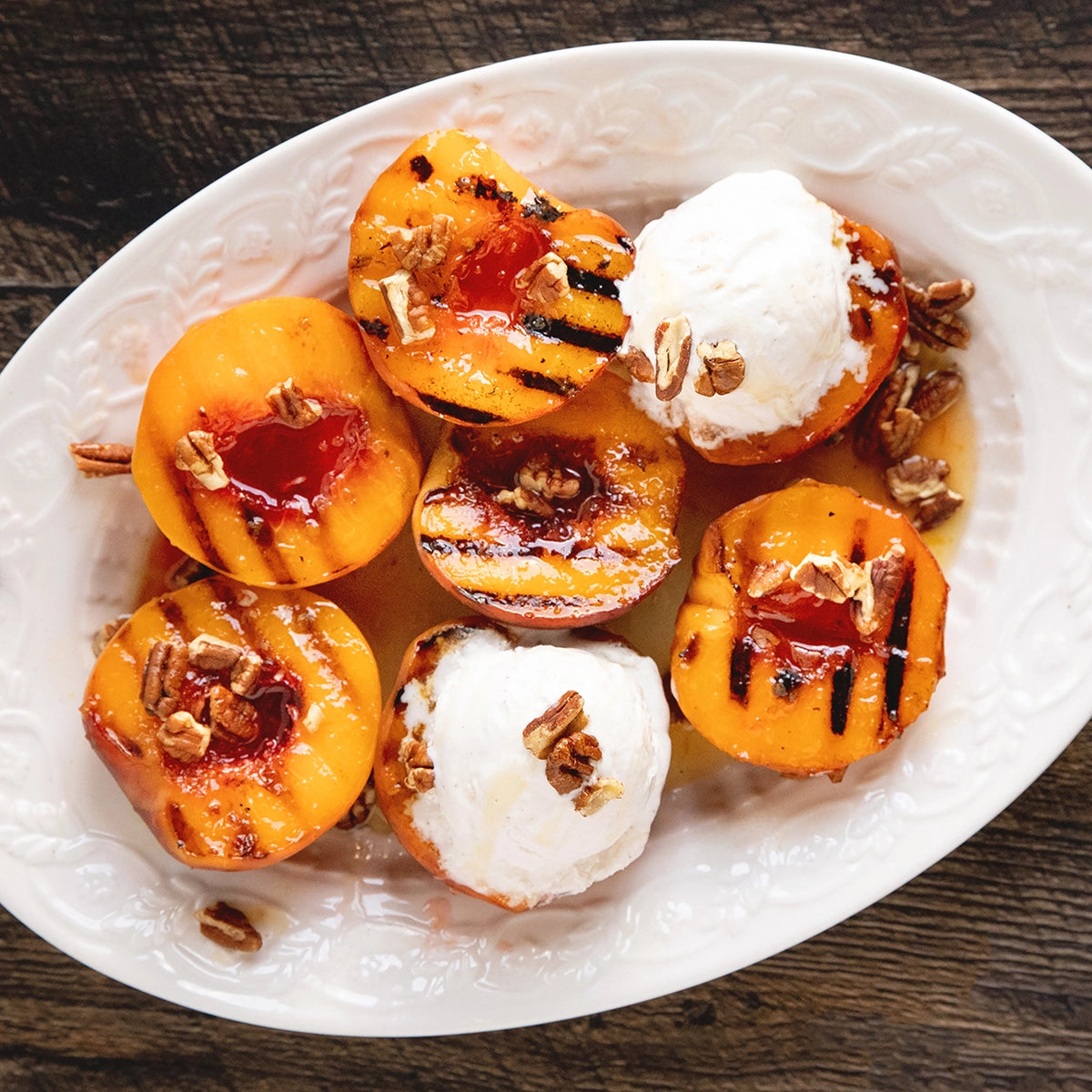 Grilled peaches with ice cream and nuts on a white plate using a sauce made with Mango Habanero Jam by Blake Hill Preserves