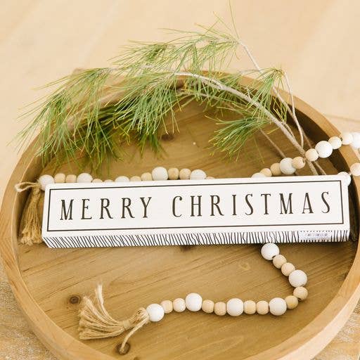 Decorative sign with 'Merry Christmas' on a wooden plate with greenery and beads.