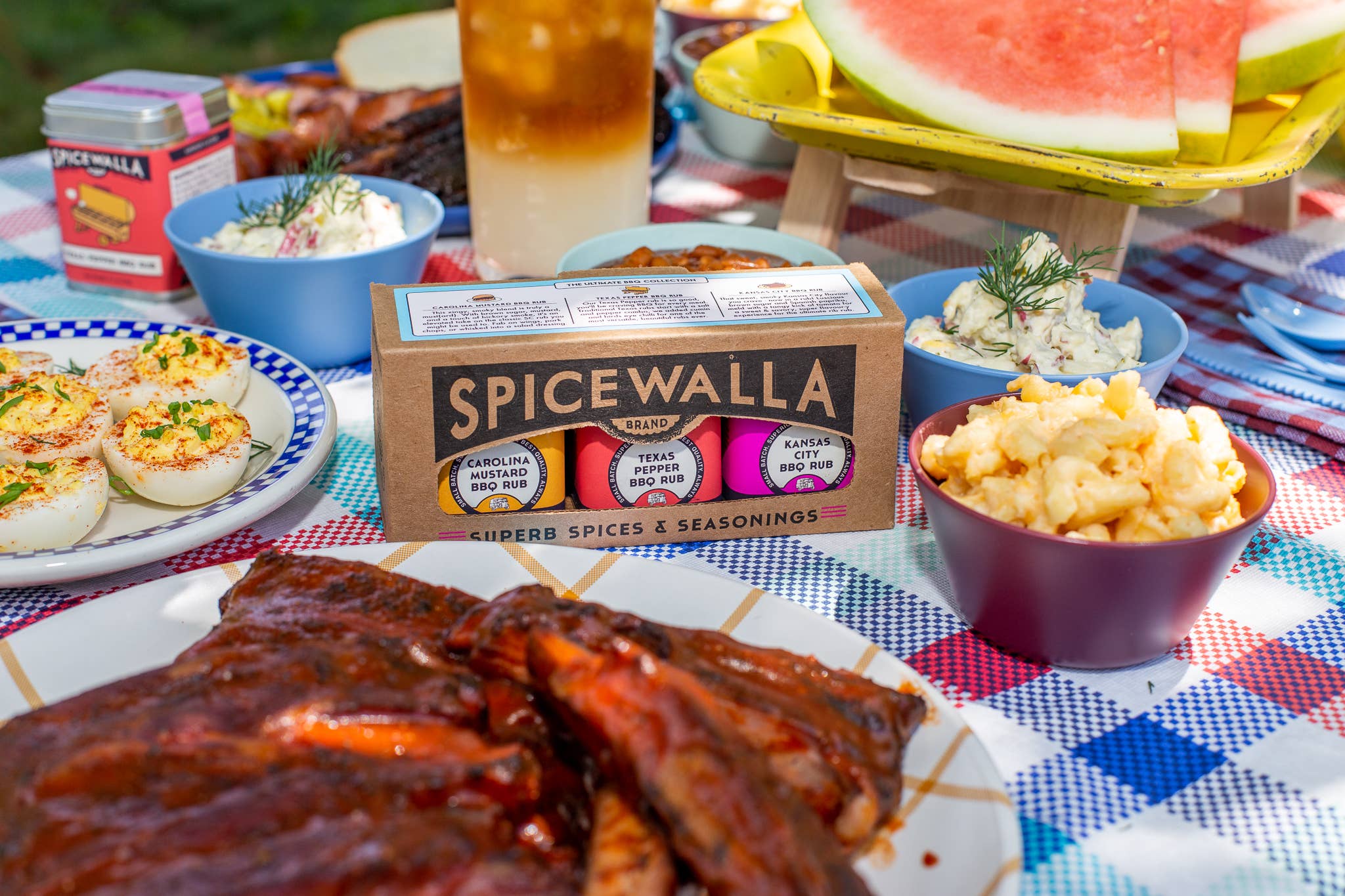 Closed up of the Spicewalla Ultimate BBQ Spice Collection set on picnic table with food and drinks