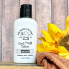 2oz Bottle of Sweater Weather Goat Milk Lotion with a sunflower and towel on a wooden background
