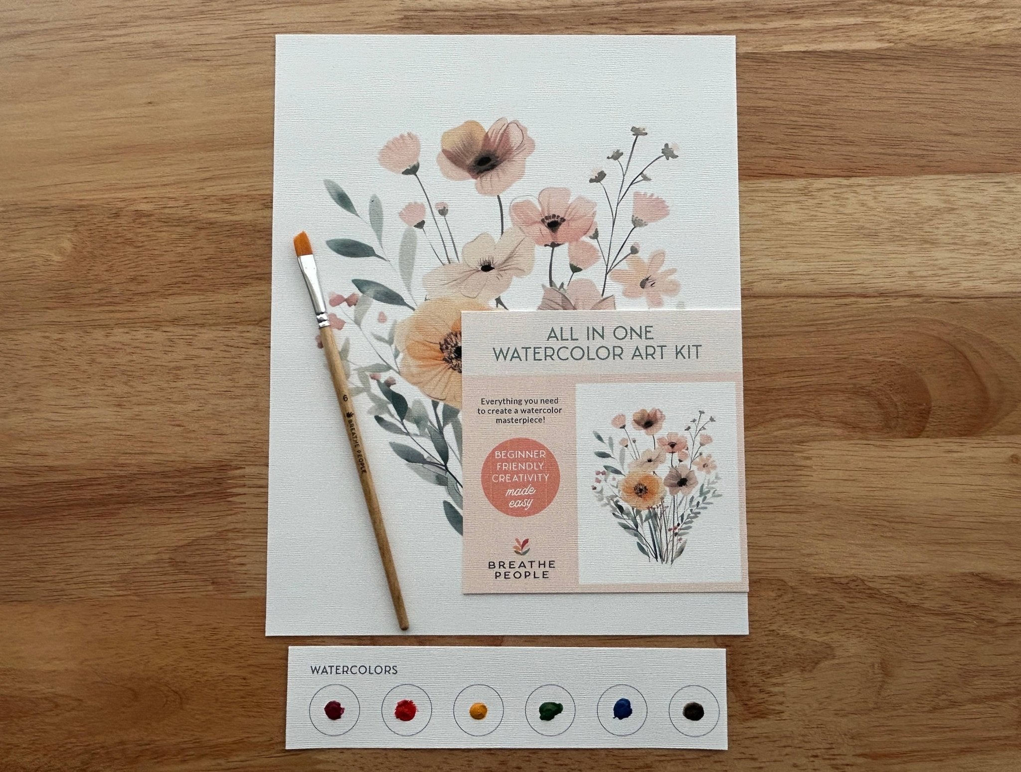 Another view of the Wildflowers Watercolor Kit by Breathe People, featuring a floral watercolor art kit with a brush and color swatches on a wooden surface.