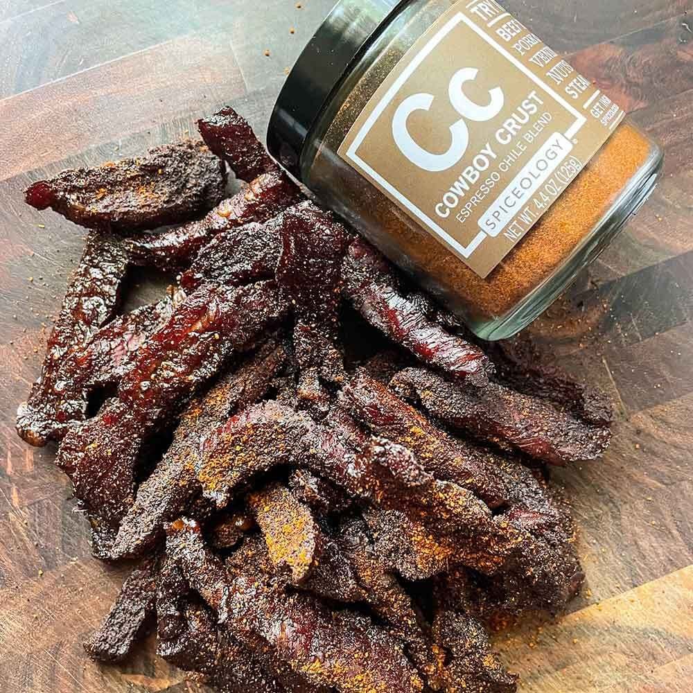 Ribs covered using Spiceology Cowboy Crust Espresso Chile Rub. The spice in a glass jar is placed next to the ribs.