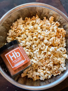 Popcorn covered using Smoky Honey Habanero. The spice in a glass jar is placed on top of the popcorn inside a bowl.